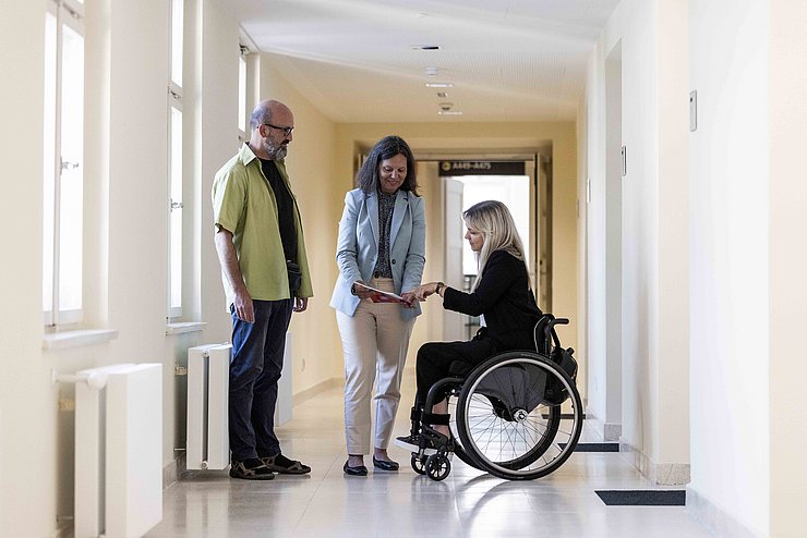 drei Personen in Gang, eine Person im Rollstuhl
