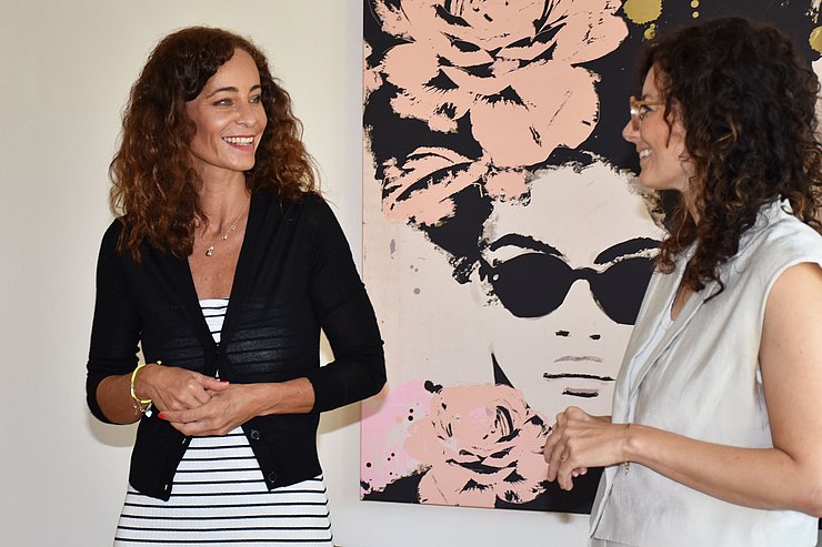 LRin und GFin lächeln, stehen vor Wand mit buntem Bild