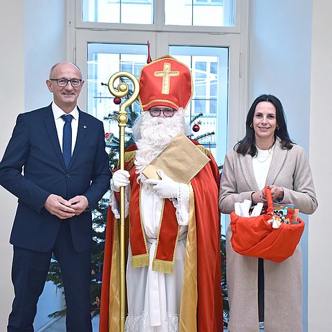 LH Anton Mattle, der Nikolaus und GFin von "Bruder und Schwester in Not" Marika Eisner zusammen vor einem Christbaum.