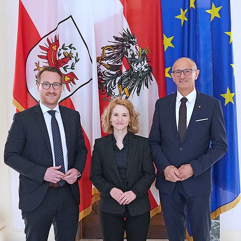 Drei Personen stehen vor Flaggen.