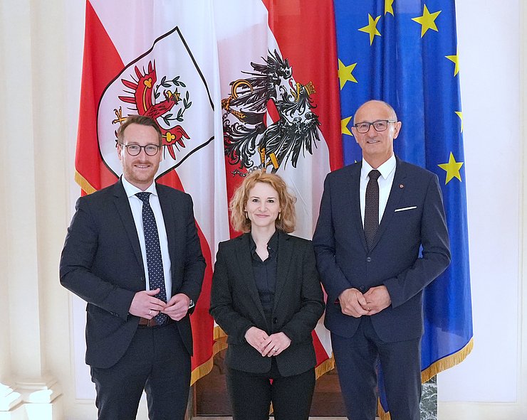 © Land Tirol/Dominik Drei Personen stehen vor Flaggen.