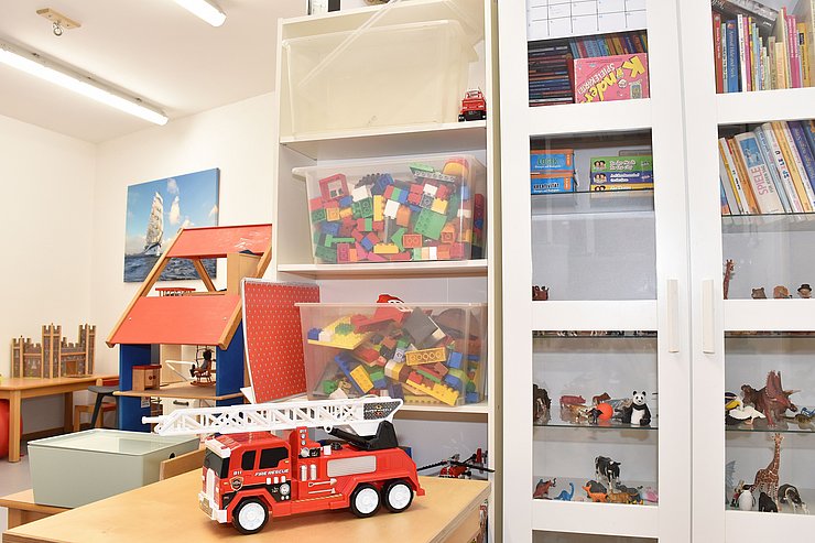 Spielzimmer: vorne auf dem Tisch steht ein Feuerwehrauto, dahinter Regale mit Bausteinen/Büchern/Tierfiguren