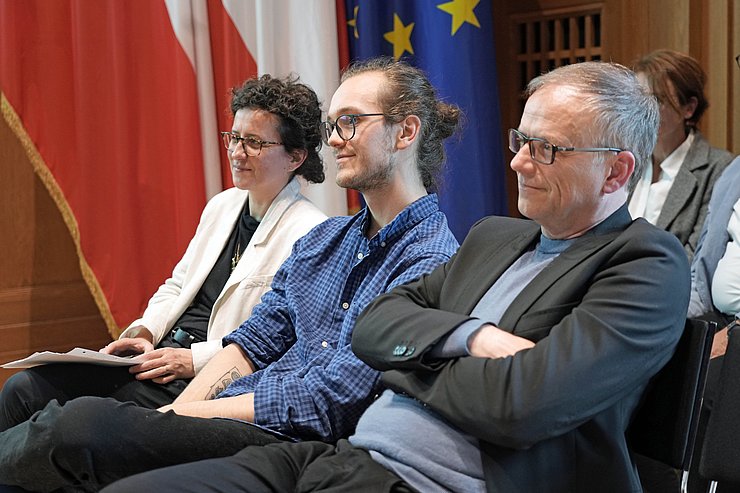 © Land Tirol/Neuner Drei Menschen sitzen auf Stühlen und lächeln.