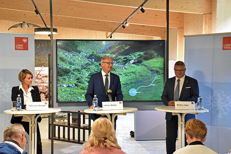 Bezirkshauptfrau Katharina Rumpf, LH Anton Mattle sowie Bürgermeister Markus Sojer stehen nebeneinander hinter weißen Tischen und beantworten die Fragen der Journalisten.