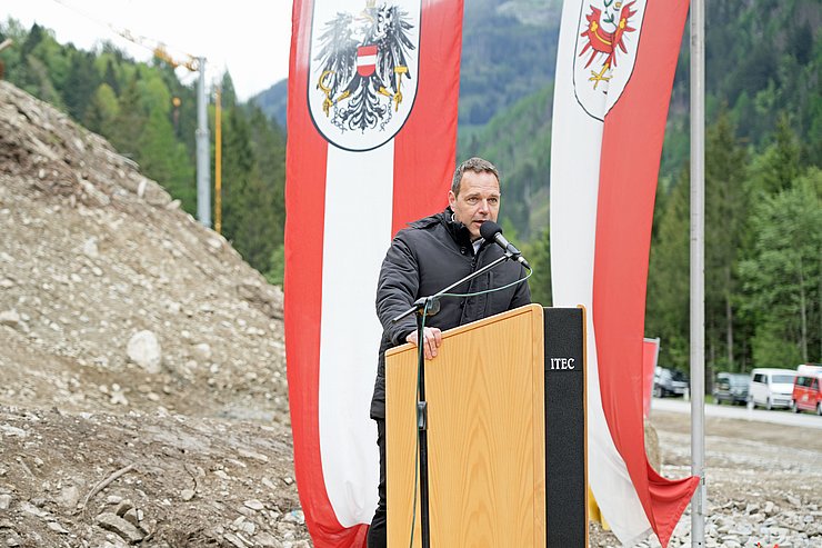 Person am Rednerpult im Freien, im Hintergrund Fahnen