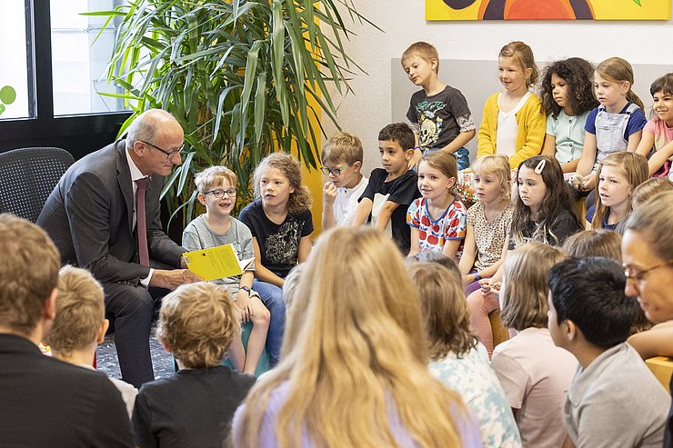 Foto von Landeshauptmann Anton Mattle vor vielen SchülerInnen während er den SchülerInnen aus einem Buch vorliest