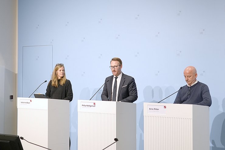 Drei Menschen bei Pressekonferenz an Podium stehend sprechend