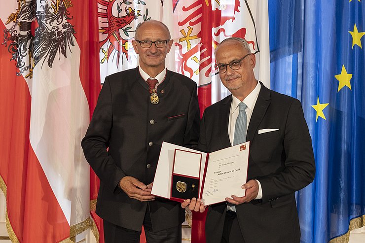 © Land Tirol/Die Fotografen links LH Mattle, rechts Herr Langer, halten gemeinsam Urkunde und Orden