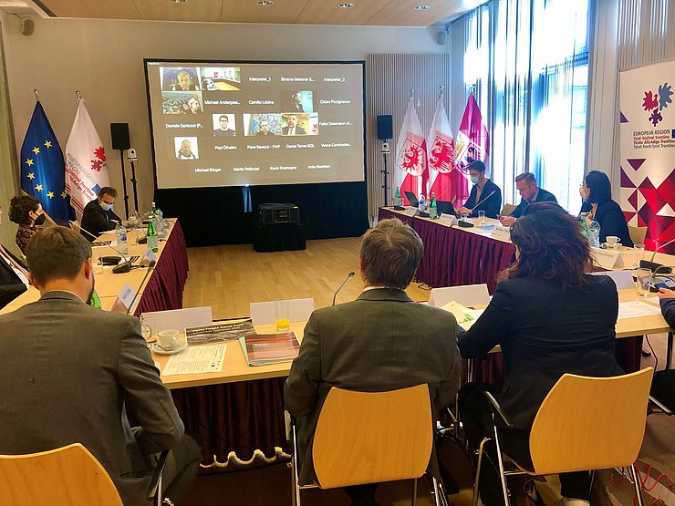 Über einen großen Bildschirm sind weitere TeilnehmerInnen zugeschaltet.