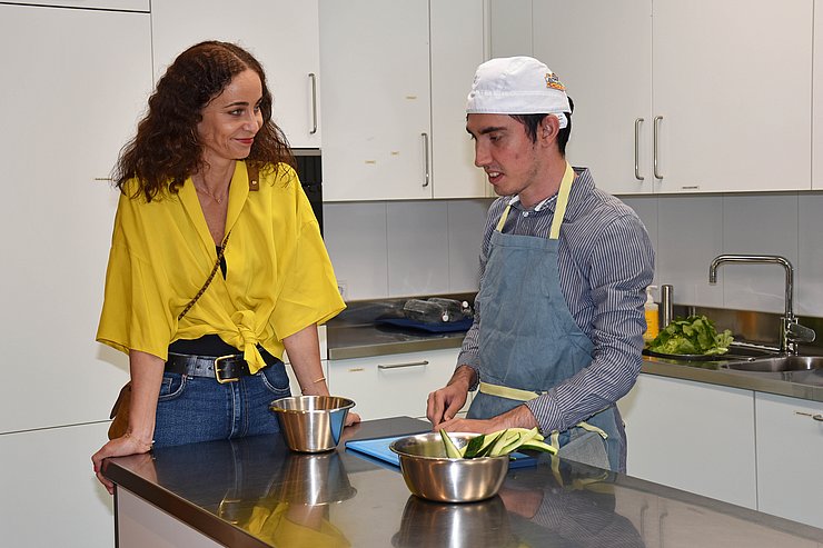 LRin sieht Klienten mit Schürze und Kochmütze dabei zu, wie er in der Küche Gurken schneidet