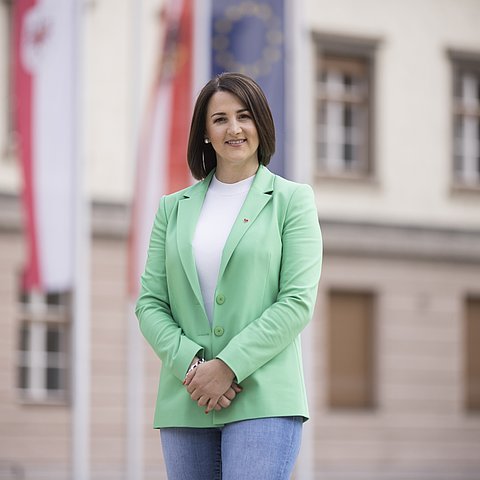 LRin Mair mit grünen Blazer vor dem Landhaus in Innsbruck: Im Hintergrund die Fahnen von Tirol. sterreich und der EU an Fahnenmästen