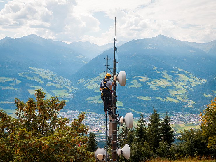 Mitarbeiter auf der Spitze des Funkmasten mit Helm und angegurtet