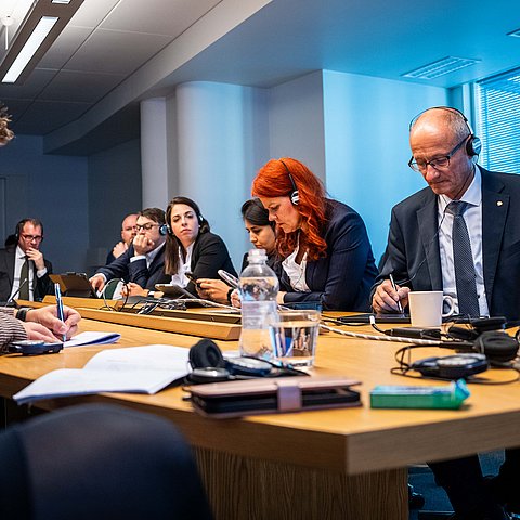 Mattle, Hagele und andere Personen an Tisch sitzend; alle haben Kopfhörer auf