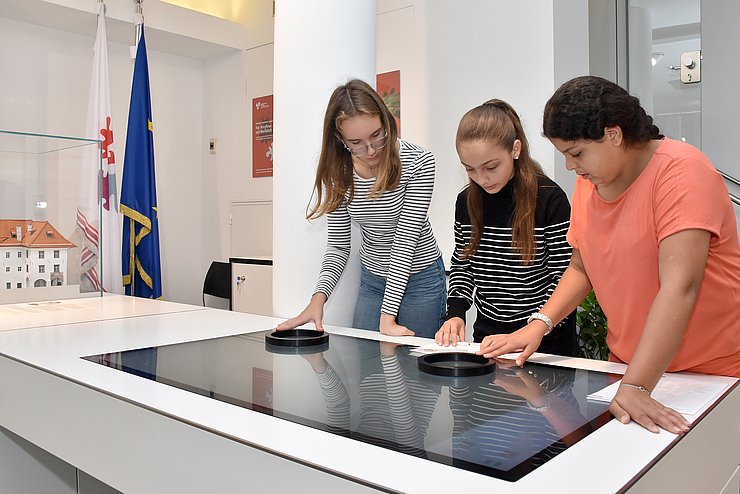 Drei Kinder schauen auf einen Bildschirm am Tisch.