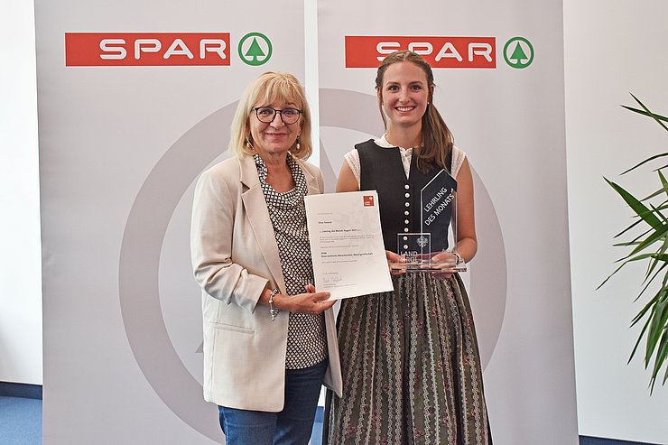 © Land Tirol/Dorfmann Landesrätin Beate Palfrader mit dem "Lehrling des Monats August 2021" Elisa Taxauer vor einem Spar-Banner