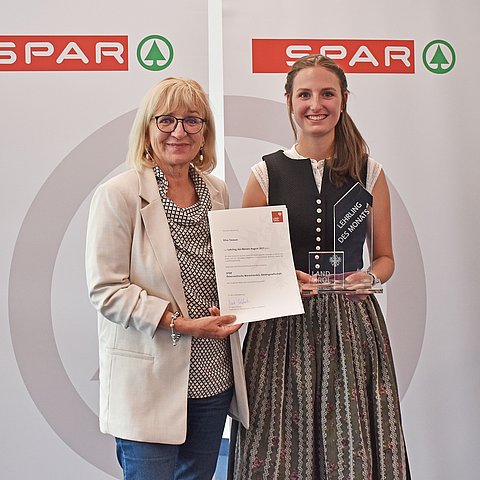 Landesrätin Beate Palfrader mit dem "Lehrling des Monats August 2021" Elisa Taxauer vor einem Spar-Banner