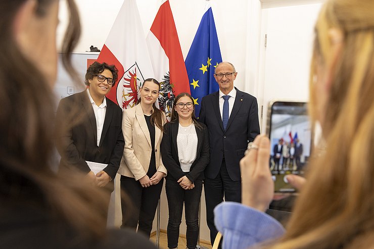 Die Schülerinnen machen vor den Flaggen ein gemeinsames Foto mit dem Landeshauptmann