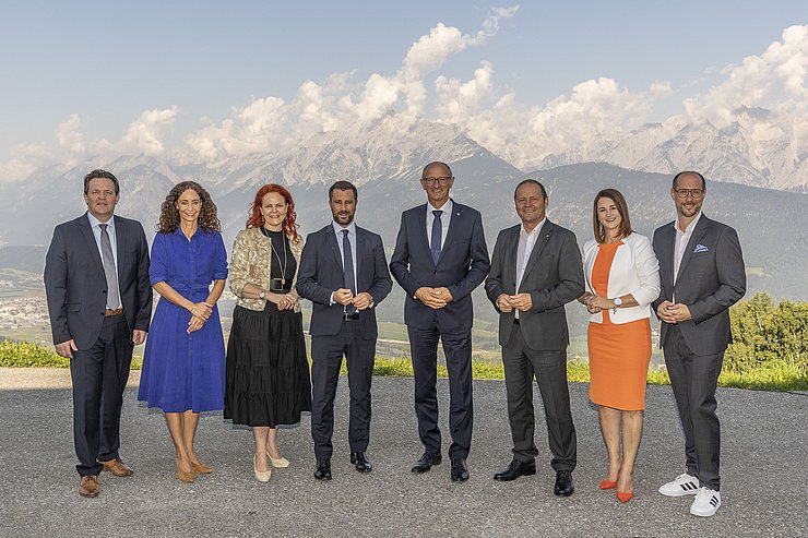 © Land Tirol/Die Fotografen Gruppenfoto der Regierungsmitglieder. Im Hintergrund ist eine Gebirgskette zu sehen.
