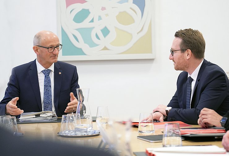 Zwei Männer sitzen an einem Tisch und reden miteinander.