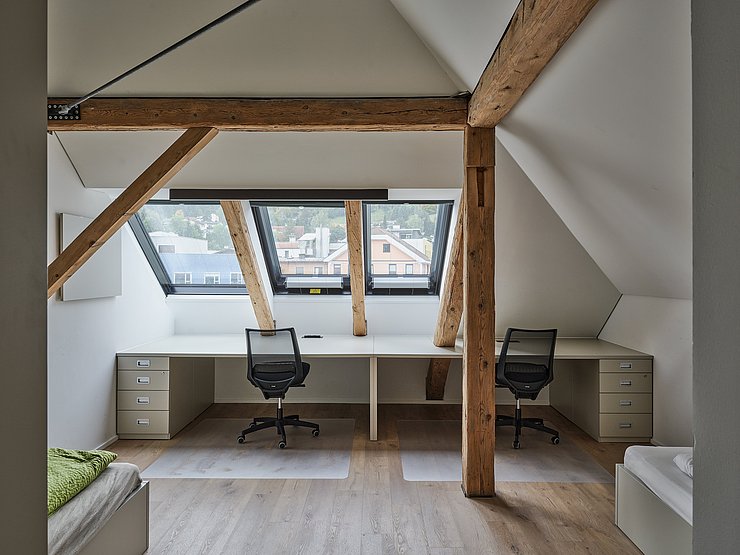 © Günter Richard Wett Dachzimmer mit Schreibtischen, Betten und sichtbaren Holzbalken