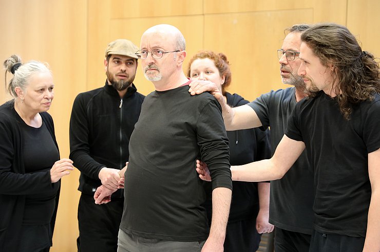 © Ursula Kronsteiner Ein Mann steht in der Mitte, mehrere Personen packen ihn mit ihren Armen.