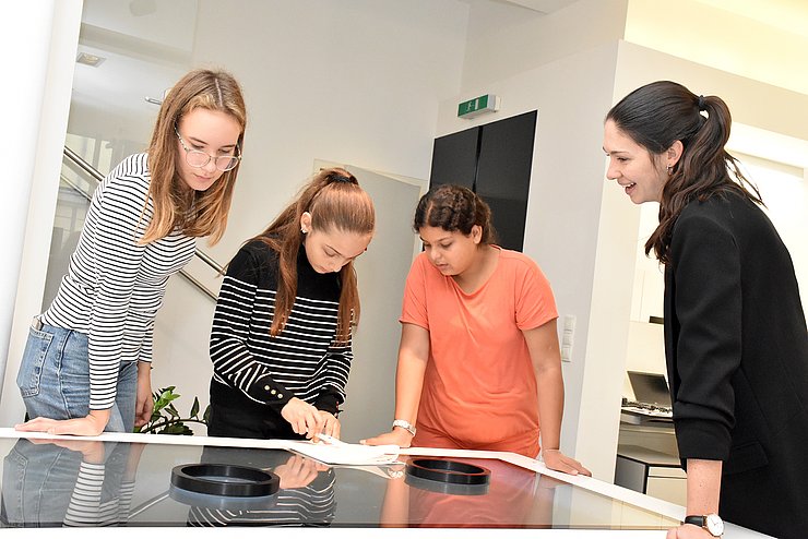 Drei Kinder und eine Frau schauen auf einen Bildschirm am Tisch.