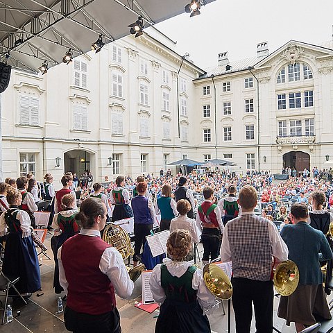 Bild vom Konzert mit den Musikerinnen und Musikern auf der Bühne und vor der Bühne mit vielen Zuschauerinnen und Zuschauern im Innenhof der Innsbrucker Hofburg.