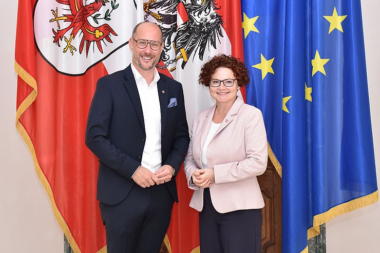 Zwei Menschen posieren vor mehreren Flaggen.