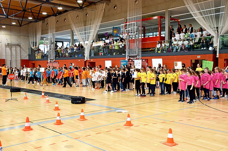 Mehrere Volksschulklassen stehen in einem Turnsaal.