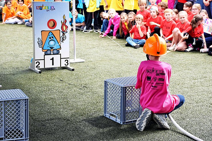 Ein Bub spritzt mit dem Feuerwehrschlauch auf eine Zieltafel.
