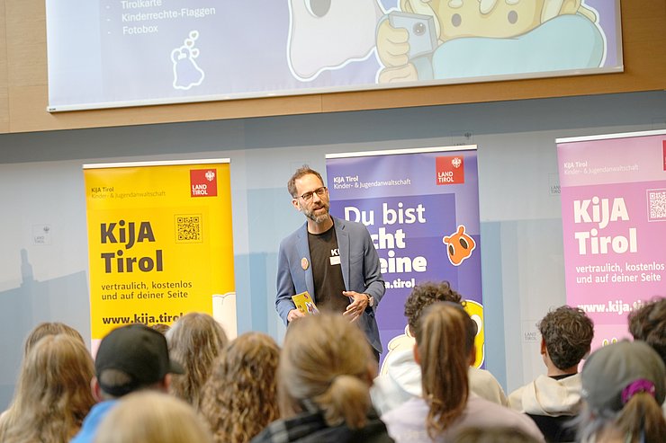 Blick über Köpfe auf Bühne mit Roll-ups, Trentini spricht