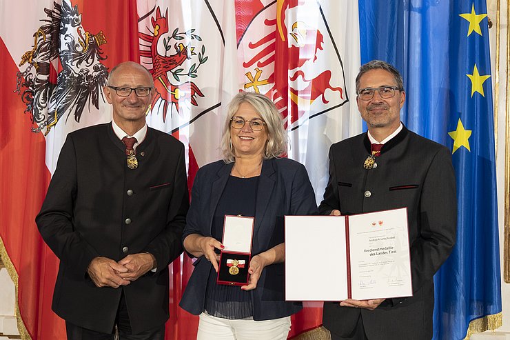 © Land Tirol/Die Fotografen links LH Mattle, in der Mitte Frau Krumschnabel und rechts LH Kompatscher, halten Medaille und Verdiensturkunde