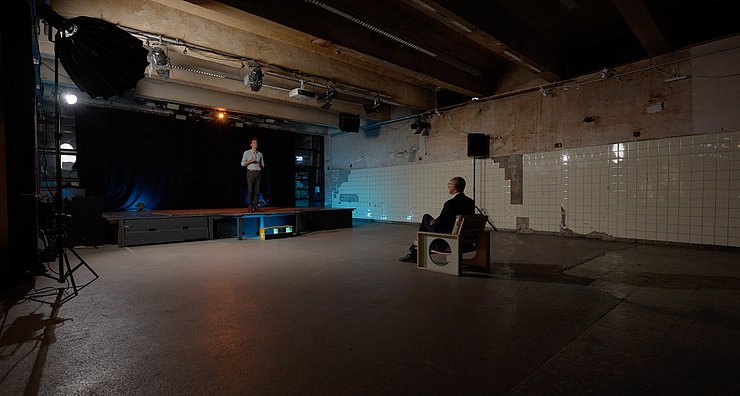 © Land Tirol Leerer Raum mit Bühne: Auf Bühne Kaschka stehend, nur ein Stuhl im Raum auf dem LH Mattle sitzt und zuhört