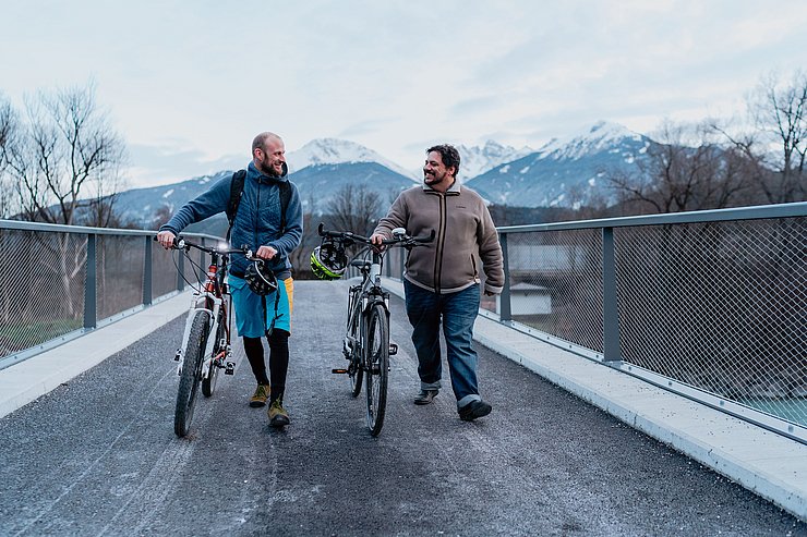Winkler und Grißmann mit Rädern über Brücke gehend