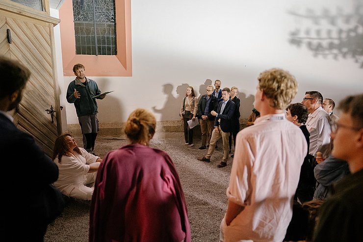 Personen stehen im Halbkreis und beobachten andere Person, die gestikuliert