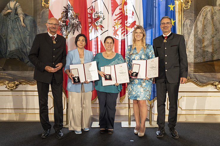 © Land Tirol/Die Fotografen rechts LH Mattle, in der Mitte die drei LebensretterInnen, halten Urkunden und Medaillen, links LH Kompatscher