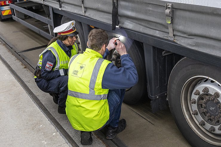 Polizistin und Techniker leuchten mit einer Taschenlampe unter einen Lkw