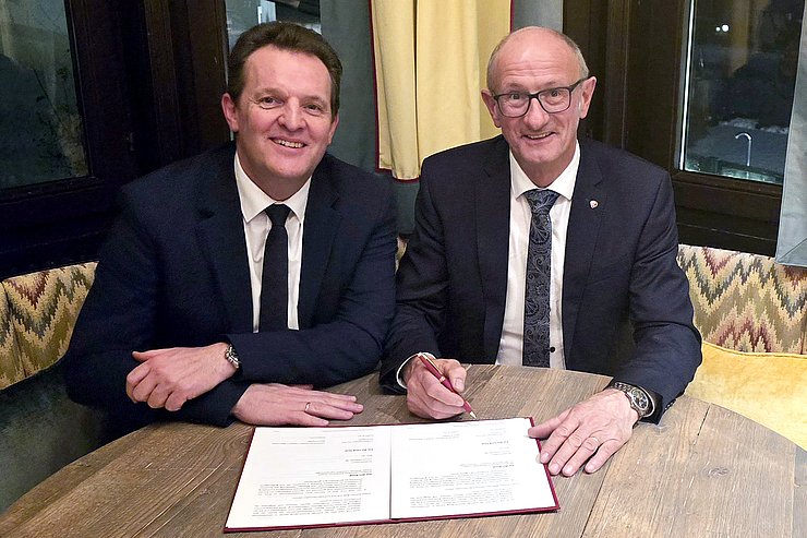 © Land Tirol Zwei Männer sitzen an einem Tisch, der rechte unterzeichnet einen Vertrag.