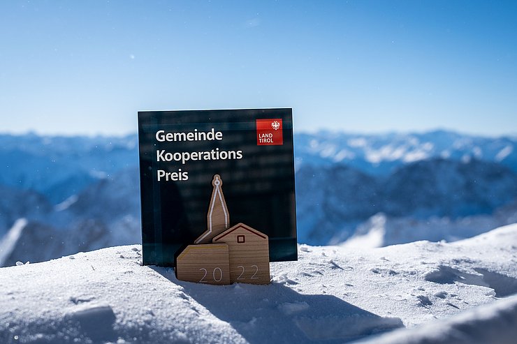 Pokal des GEKO auf Schnee stehend mit Bergen im Hintergrund