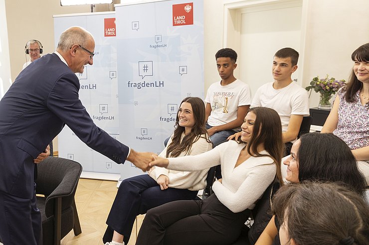 Der Landeshauptmann schüttelt einer sitzenden Schülerin die Hand
