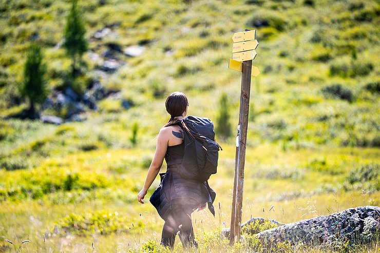 © Marco Christanell Eine Frau auf einem Wanderweg neben gelben Wegweisern