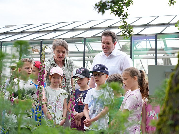 Zwei Erwachsene und mehrere Kinder, im Hintergrund ein Glashaus