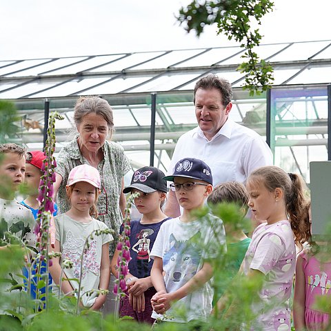 Zwei Erwachsene und mehrere Kinder, im Hintergrund ein Glashaus