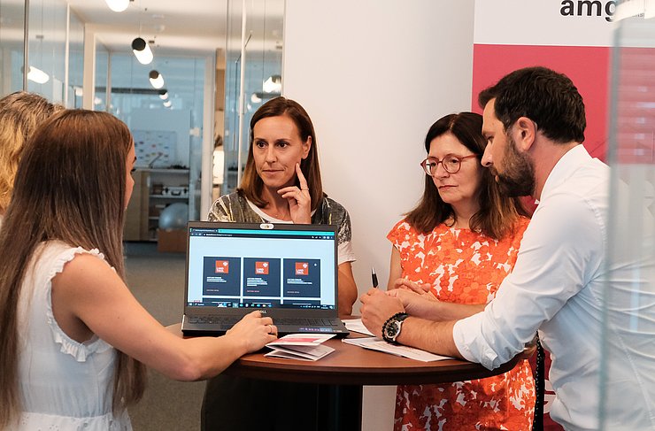 Dornauer und drei Frauen um Tisch stehend auf Laptop schauend