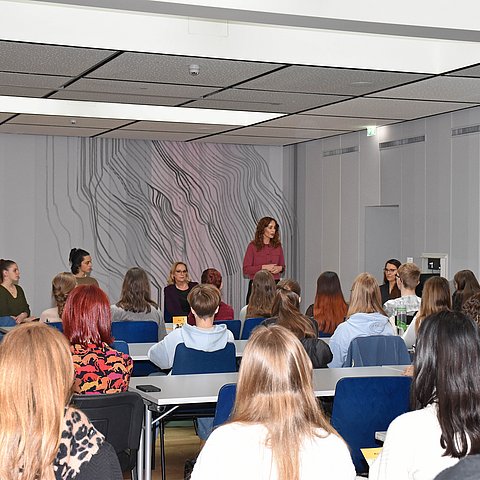 Blick von hinten über die Köpfe der SchülerInnen hinweg auf das Podium, wo gerade LRin Pawlata spricht