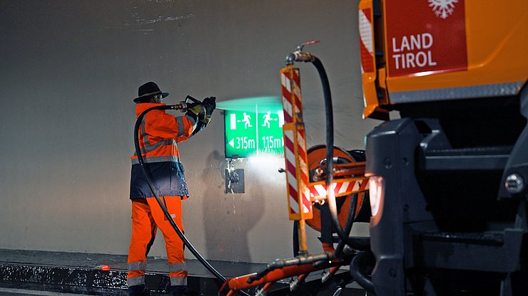 © Land Tirol/Rauch Mann spritzt mit Schlauch Fluchwegzeichen im Tunnel ab
