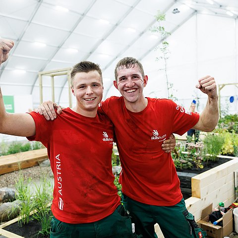 Die beiden Gewinner in einem Gewächshaus: Sie halten sich in den Armen und strecken jeweils eine Faust in den Himmel