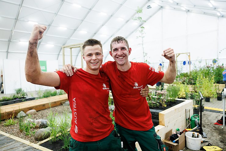 Die beiden Gewinner in einem Gewächshaus: Sie halten sich in den Armen und strecken jeweils eine Faust in den Himmel