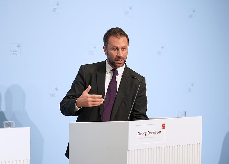 © Land Tirol/Neuner Ein Mann steht an einem Rednerpult und gestikuliert mit der rechten Hand.