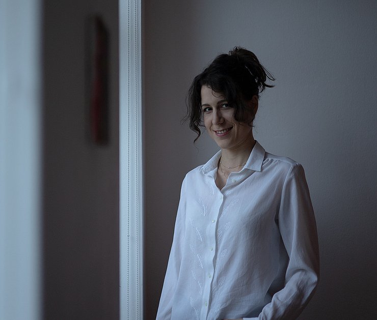 Die Künstlerin Sophia Mairer trägt eine weiße Bluse und hat dunkle, hochgesteckte Haare.
